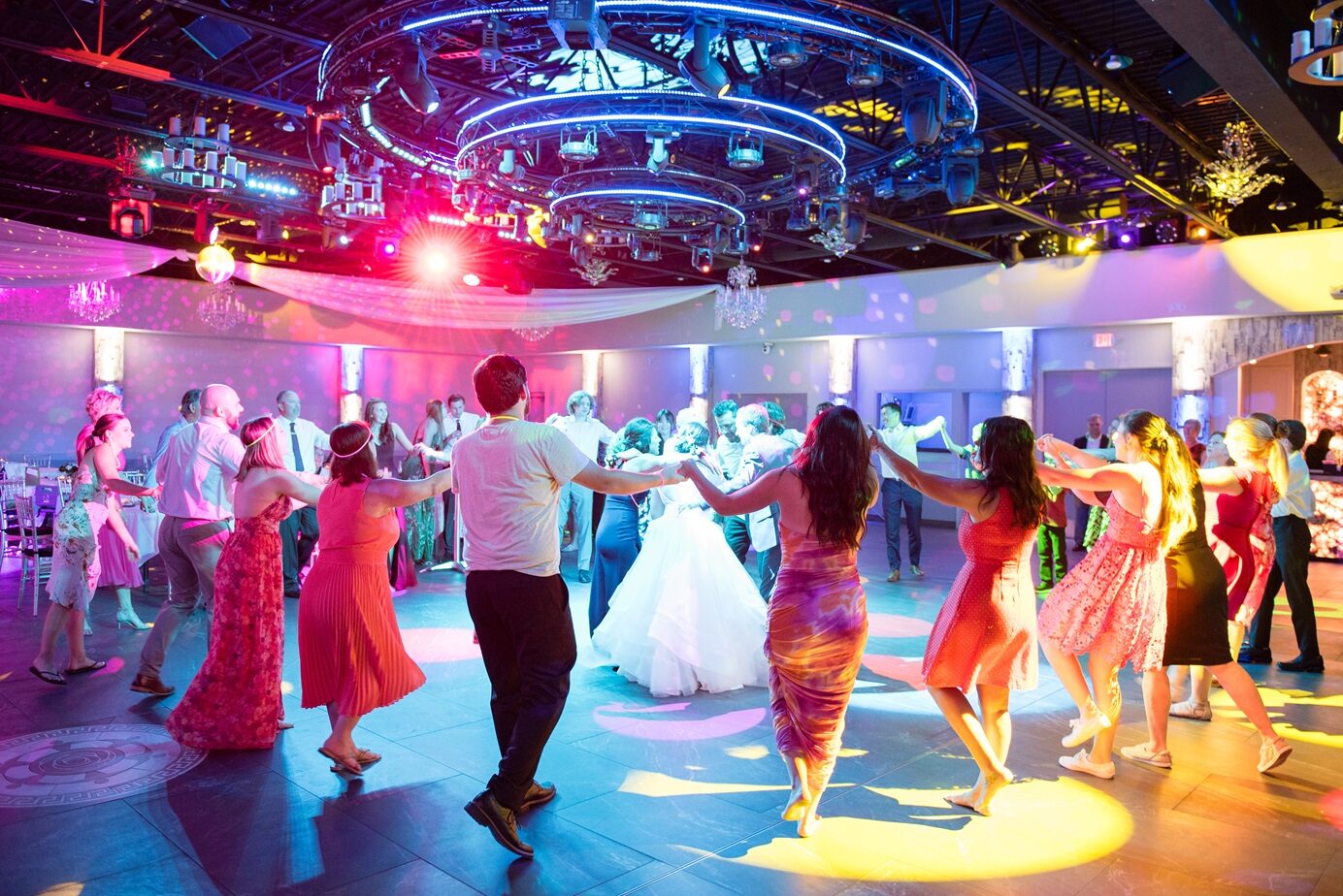 Royal Cliff dance floor in Eagan, MN — wedding guests circled around the bride and groom under colorful stage lighting and chandeliers