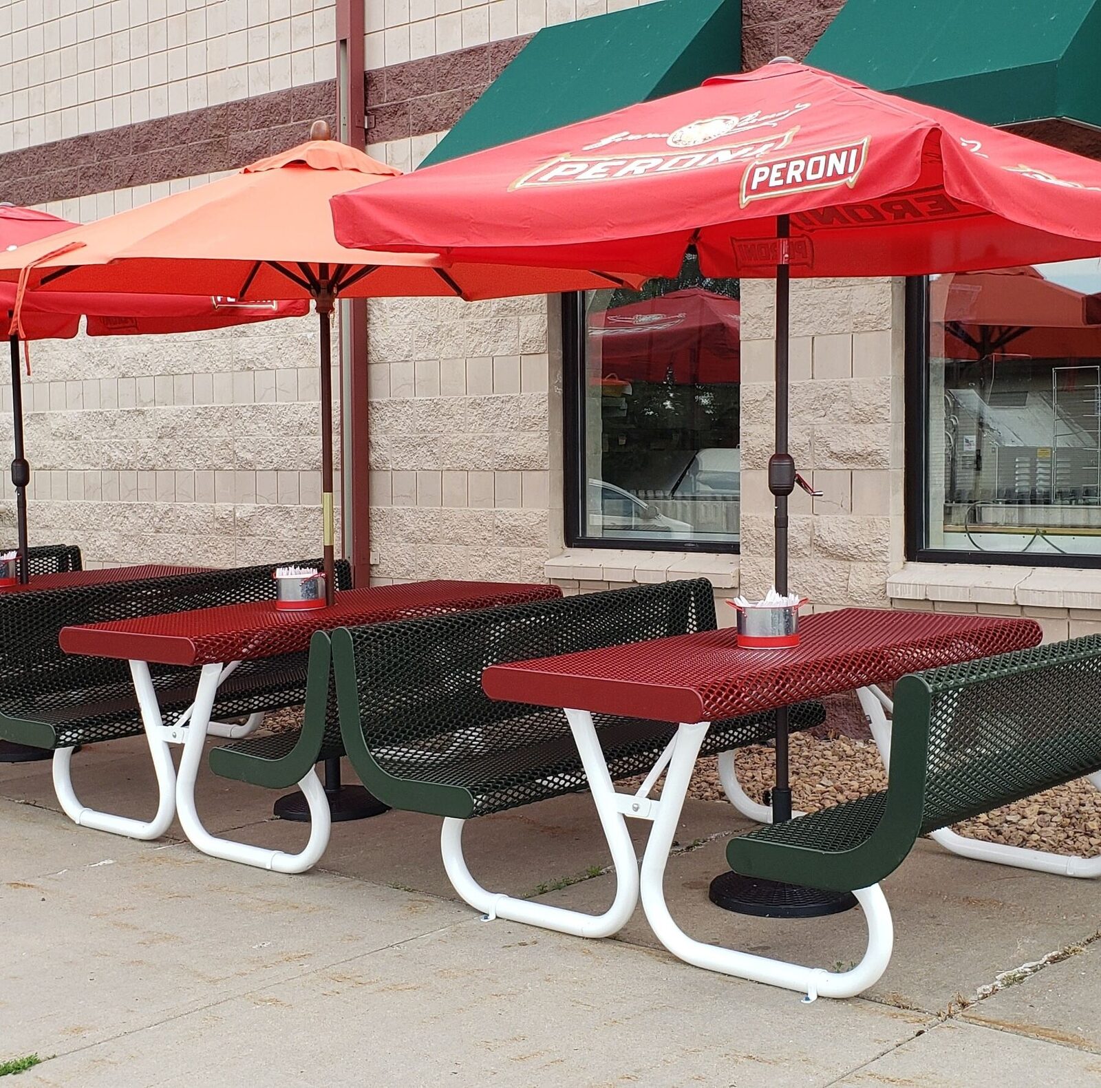 Four outdoor benches with red Peroni umbrellas in front of Brianno's Deli Italia